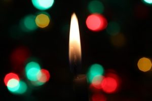 Image of candle burning with Christmas lights in the background
